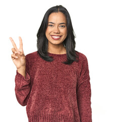 Wall Mural - simple portrait of a young latina joyful and carefree showing a peace symbol with fingers.