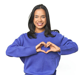Wall Mural - simple portrait of a young latina smiling and showing a heart shape with hands.