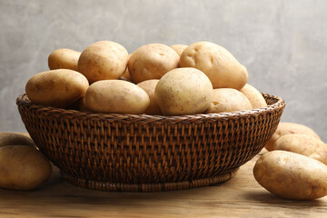 Wall Mural - Many fresh potatoes in wicker basket on wooden table, closeup