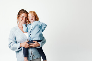 Wall Mural - Mother and daughter bonding woman embracing little girl in stylish blue sweater and gray pants