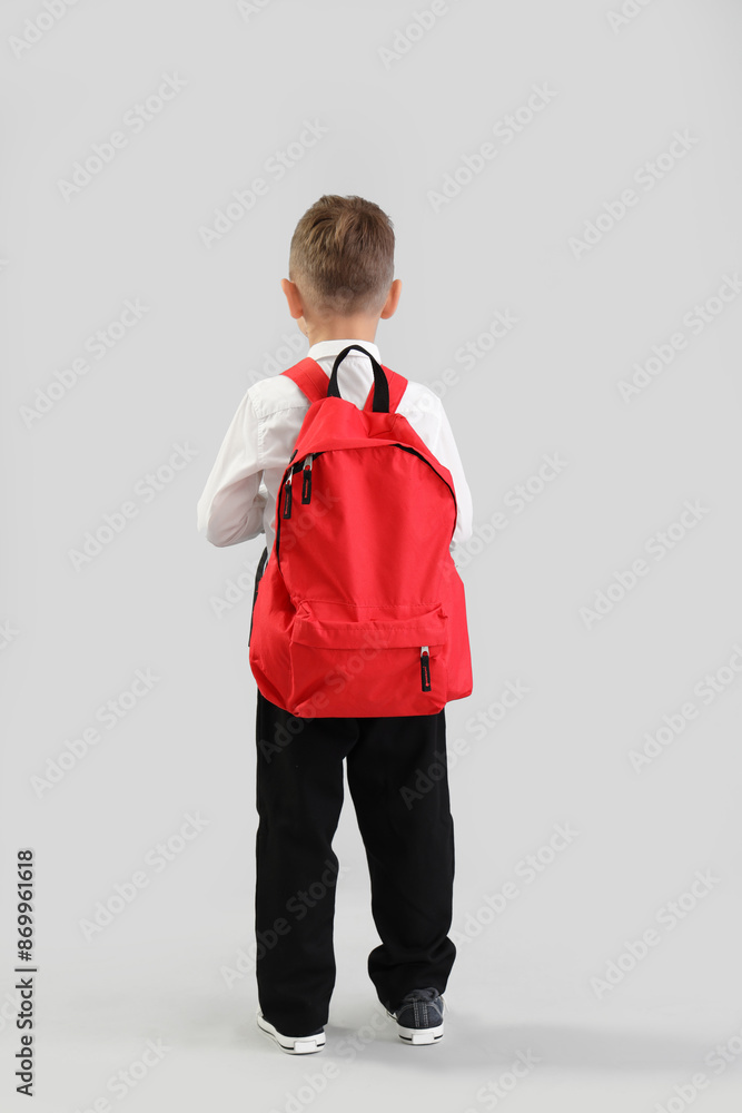 Little schoolboy with red backpack on grey background, back view