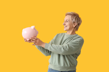 Poster - Beautiful mature woman with pink piggy bank on yellow background