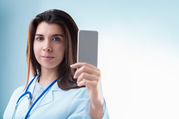 Female doctor showing smartphone with empty screen on blue backg