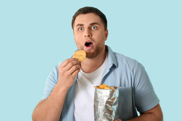 Sticker - Handsome young shocked man with tasty potato chips on blue background