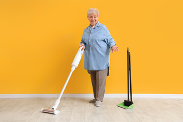 Sticker - Senior woman with vacuum cleaner rejecting broom near yellow wall