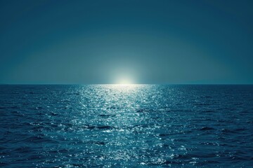 Wall Mural - A calm ocean with a sun rising in the distance. The sky is dark blue and the water is a deep blue color