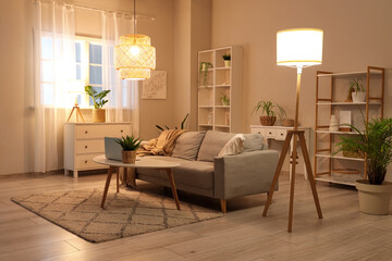 Poster - Beautiful interior of modern living room with sofa, armchair, coffee table with laptop and glowing lamps