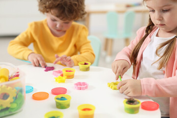 Poster - Little children modeling from plasticine at white table in kindergarten, closeup