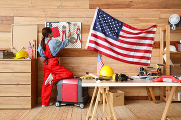 Sticker - Female worker taking tool from peg board near USA flag in workshop. Labour Day celebration