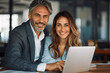 © btiger - Happy business partnership mature Latin man and European woman working together on laptop at office table discussing project professional colleagues teamwork