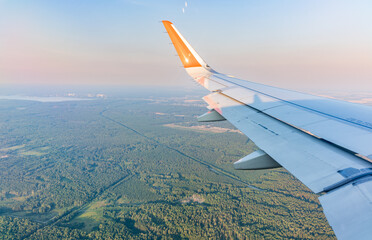 View of airplane wing, blue skies and green land during landing. Airplane window view.