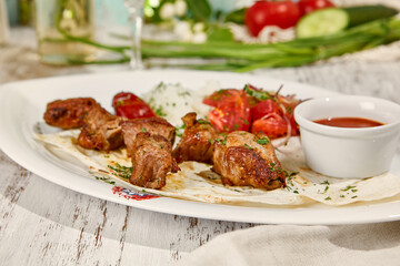 Wall Mural - Pork Shashlik with Lavash, Sauce, and Fresh Vegetable Salad in Sunlight on Wooden Table