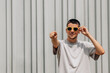 © carballo - young man with sunglasses in summer on the street wall pointing