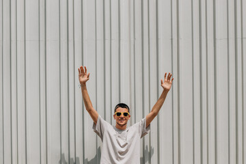 Poster - young man in sunglasses in summer on the street wall with arms raised