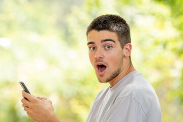 Wall Mural - young man with mobile or cell phone outdoors with surprised expression