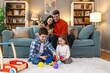 © Graphicroyalty - Cute kids playing while parents relaxing sofa at home together, smiling active boy entertaining with toy car near his sister on floor, happy family spending time together in living room on weekend