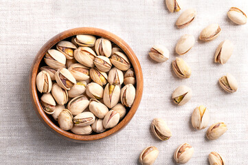 Wall Mural - Pistachios in their shells, roasted and salted, in a wooden bowl on linen fabric. Crunchy roasted fruits of Pistacia vera, with opened shells and seeds within. Ready-to-eat snack food. Close-up. Photo