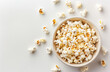 © reddish - A close-up overhead shot of a bowl filled with freshly popped popcorn, surrounded by scattered popcorn kernels on a white background