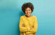 © Aytana - Happy joyful dark skinned woman laughs happily keeps arms folded and expresses positive emotions grins from happiness dressed in casual jumper isolated on blue background has fun or hears funny joke