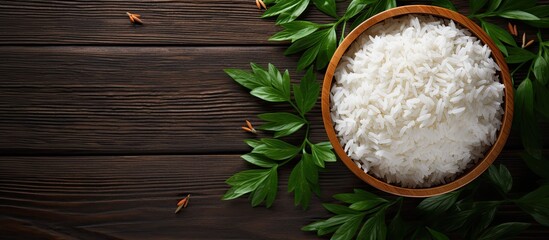 Poster - Top-down perspective of Jasmine rice displayed on a dark wooden surface among lush green plants, featuring jasmine rice served in a wooden bowl with copy space image.
