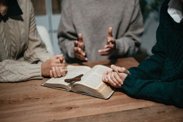 Wall Mural - Group of Christians sit together and pray around a wooden table with blurred open Bible pages in their homeroom.