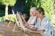 © ulza - Two happy middle aged woman smiling while drawing watercolor as a recreational activity or therapy outdoors together with the group of retired women. KnowledgeForAll