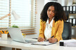 © Prathankarnpap - ConcentratedAfrican American businesswoman doing paperwork and using laptop at her workplace