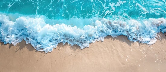 Wall Mural - Turquoise ocean waves gently caressing a sandy beach, captured in a high-angle copy space image.