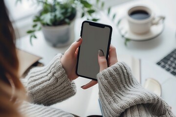 Top view of female hands holding smartphone with blank screen on white wooden table background