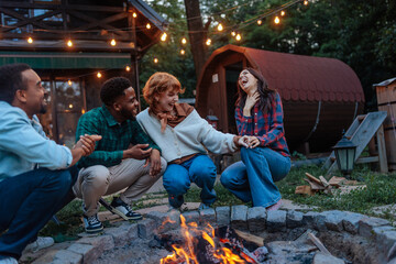 four people having fun and laughing next to a burning fire pit