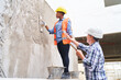 © Robert Kneschke - Senior male builder gesturing while talking to female bricklayer plastering wall with mortar at construction site