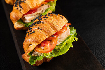 Wall Mural - Tasty croissant with chicken, tomato and salad on black table