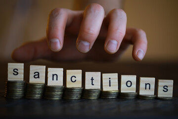 Poster - Word Sanctions made of wooden block letters with coins stacks