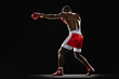 © master1305 - Side view image of athletic muscular man with sweating shirtless body, boxer in red shorts and gloves training isolated on black background. Concept of professional sport, active lifestyle, strength