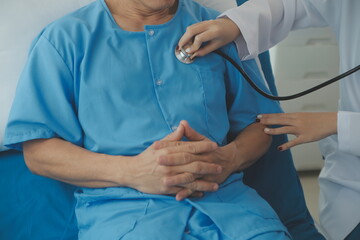 Wall Mural - Doctor using stethoscope to listen senior man heart during examination in hospital room and wearing visor as safety precaution against coronavirus. Medical control for infections, disease.