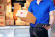 © Katcha - A man in a blue shirt is holding a cardboard box and a tablet