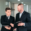 © Katcha - Two men in suits are discussing something, one of them is holding a clipboard