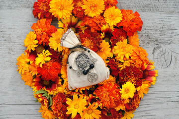 Poster - magic witch's bag with amulets and colorful flowers on wooden background close up. esoteric concept. Floral magic, witchcraft, occult wiccan ritual. top view