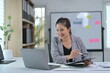 © Parichat - Businesswoman Working on Laptop in Modern Office with Documents and Whiteboard in Background