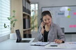 © Parichat - Young Professional Woman Working in Modern Office on Phone Call with Documents and Tablet
