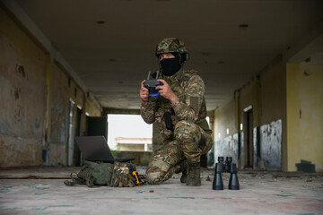 Wall Mural - Military mission. Soldier in uniform with drone controller, laptop and binoculars inside abandoned building