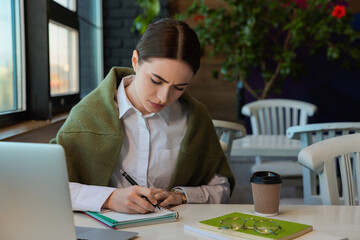 Wall Mural - Young female student with laptop studying at table in cafe