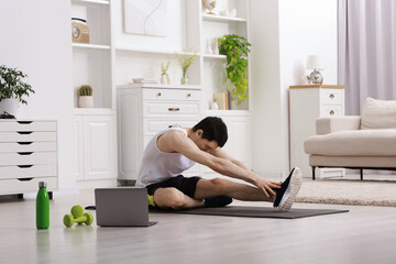 Online fitness trainer. Man doing exercise near laptop at home