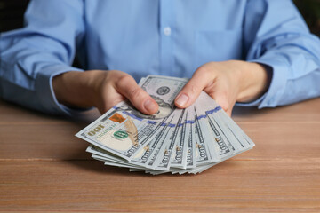 Wall Mural - Money exchange. Woman holding dollar banknotes at wooden table, closeup