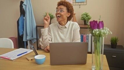 Sticker - Cheerful african american woman, sitting at home, exclaims eureka! pointing finger up, showing the number one for her brilliant idea and smiling at her success.