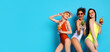 © Prostock-studio - Three young women in swimsuits pose together against a bright blue background. They are all smiling and holding cocktails, copy space