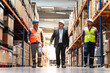 © bulentbaris - Manager and factory employees work together to warehouse aisle. Three men they are wearing hard hats and reflective vests.