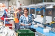 © bulentbaris - A woman wearing a blue and white plaid shirt is working on an assembly line. She is holding a circuit board in her hands. There are many bins and other electronic parts on the table in front of her.