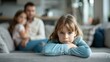 © Irina Ukrainets - Sad child laying her arms on couch while parents blurred. Focus on child face. Family dynamic, separation, and emotion concept. Close-up, horizontal photo for emotional storytelling. AI