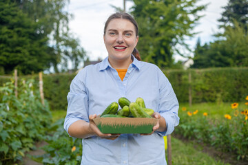 Young woman, farmer, worker holding in hands homegrown harvest of fresh orange cucumber. Private garden, orchard, natural economy, hobby and leisure concept. High quality photo